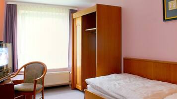 A hotel room with a bed, a chair, a desk, and a radiator.