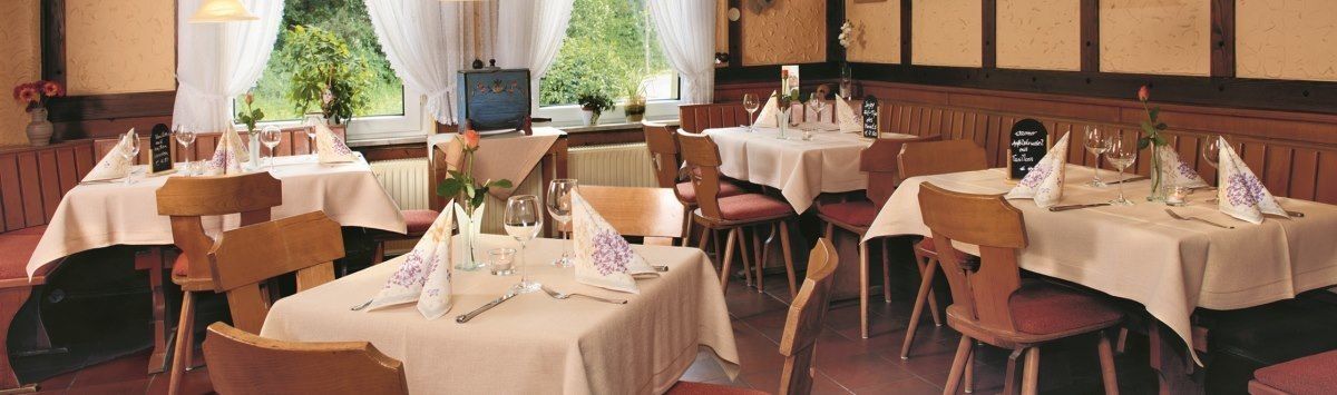 A restaurant with multiple tables set for dining, each with white tablecloths and neatly arranged cutlery.