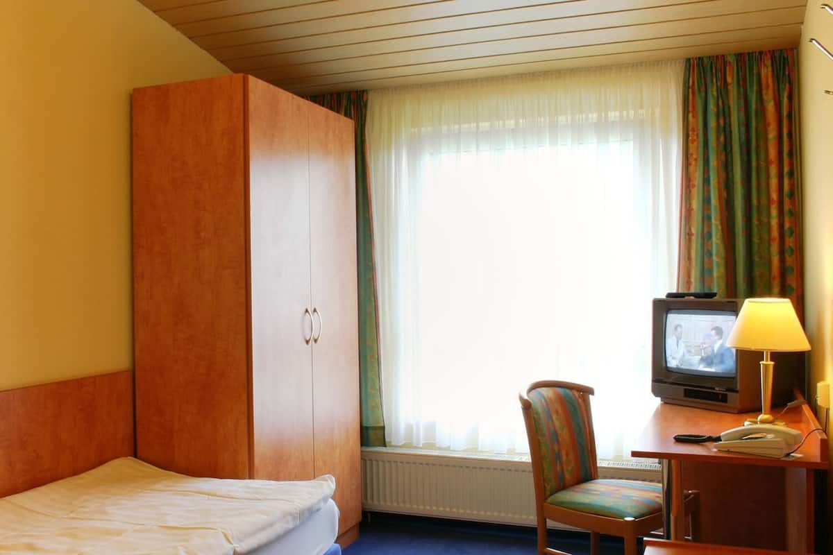 Una habitación de hotel con una cama, un armario de madera, un escritorio con televisor, una silla y una ventana con cortinas.