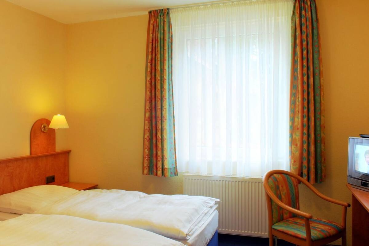 Una habitación de hotel con dos camas, un escritorio con televisor, una silla y una ventana con cortinas.