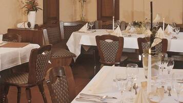 Un restaurante con varias mesas dispuestas para comer, cada una con manteles blancos, velas y cubertería ordenada.