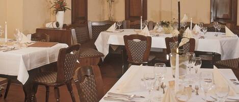 A restaurant with multiple tables set for dining, each with white tablecloths, candles, and neatly arranged cutlery.