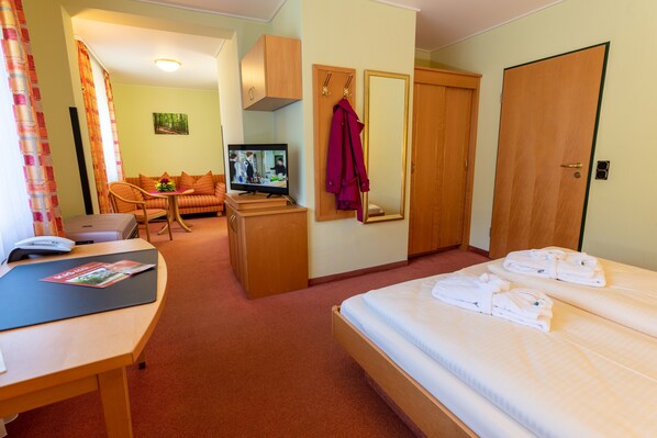 A hotel room with a bed, a desk with a computer, a TV, a sofa, and a wardrobe. - Kishotel Am Kurpark (Bad Soden-Salmuenster)