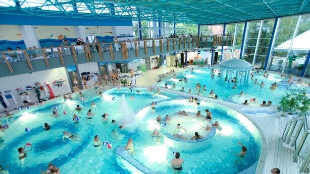 Un vaste espace intérieur abritant plusieurs piscines et doté d’une terrasse supérieure couverte.