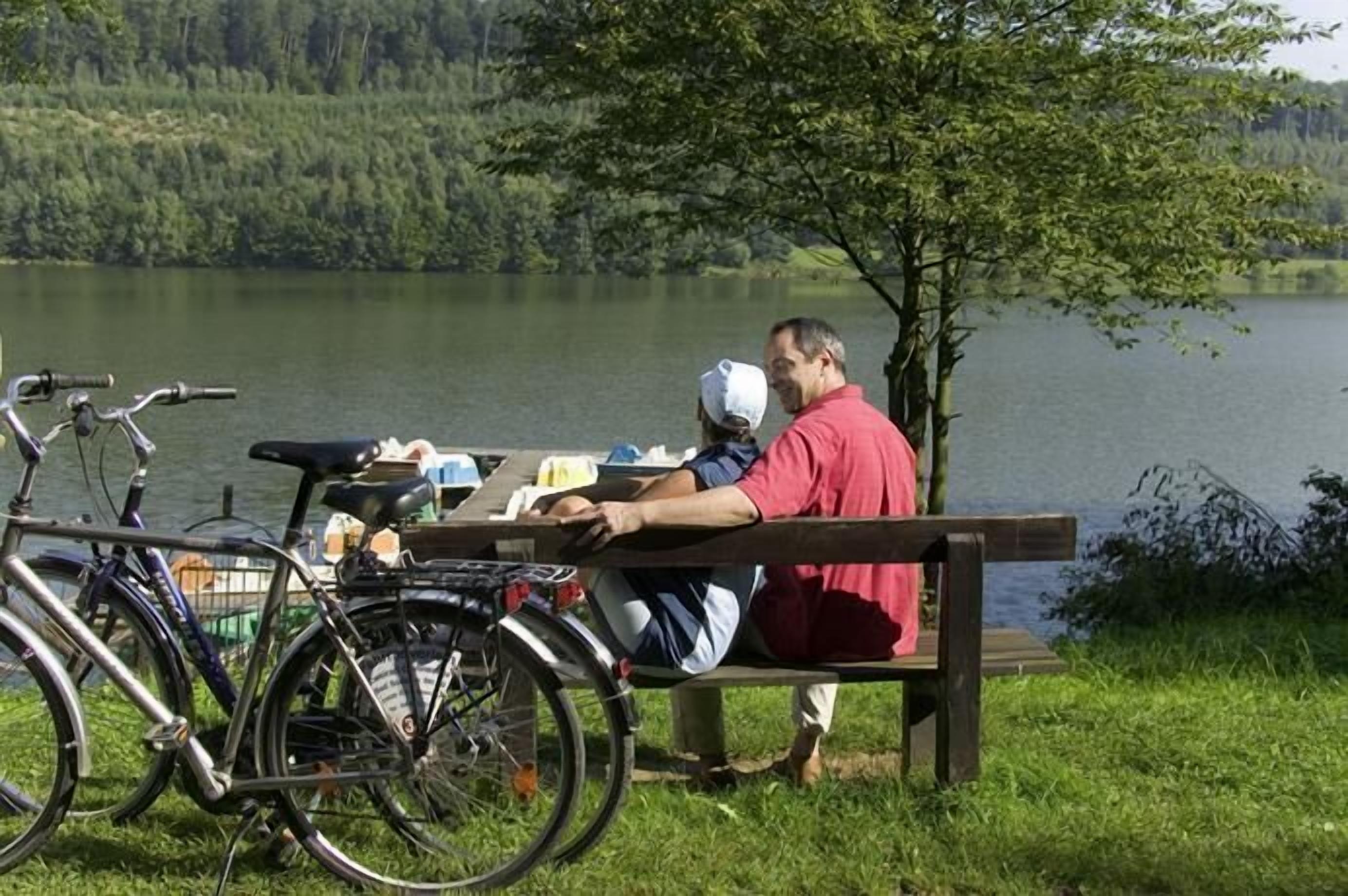 Un hombre sentado en un banco junto a un lago, con bicicletas estacionadas cerca.