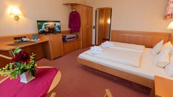 Une chambre d’hôtel comprenant un lit, un bureau avec une télévision, une armoire et une petite table sur laquelle est posé un vase de fleurs.