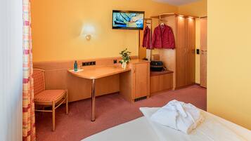 A hotel room with a bed, a desk, a chair, a TV, and a wardrobe.