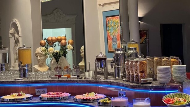 A buffet setup with various food items, a statue, and a mirror. - Gästehaus Kral (Erlangen)