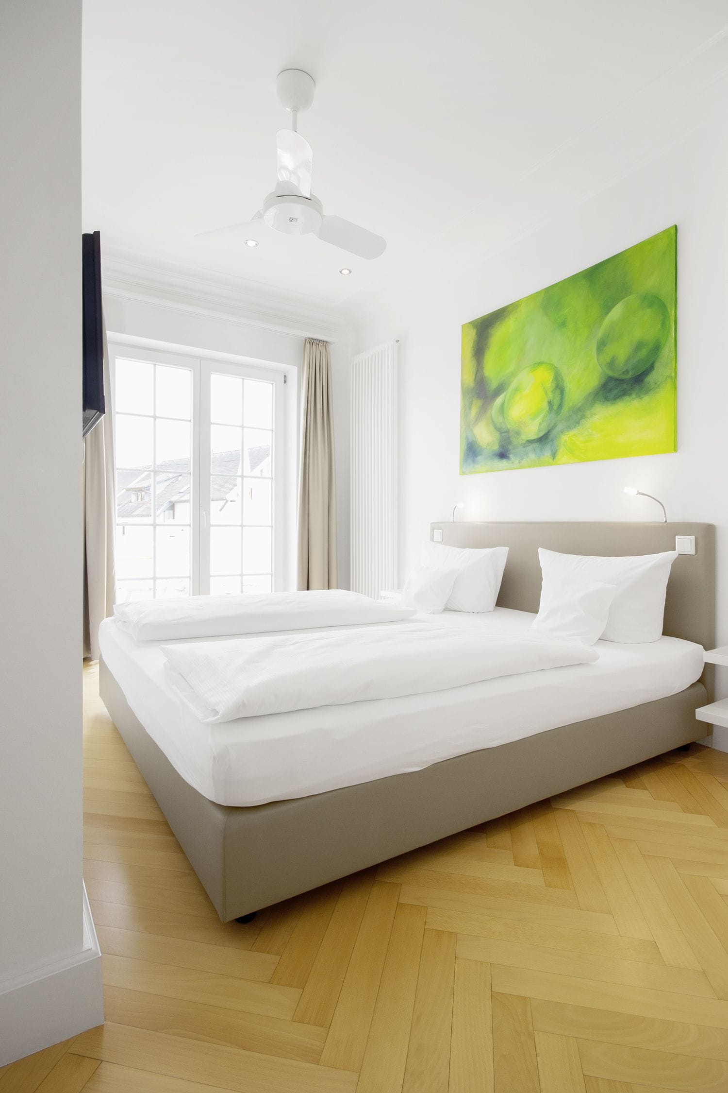 Una habitación de hotel moderna con una cama grande, un ventilador de techo y una ventana con cortinas.