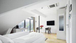 Un dormitorio moderno con una cama grande, un escritorio y una silla, un televisor montado en la pared y una puerta que da a otra habitación.