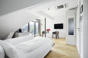 Un dormitorio moderno con una cama grande, un escritorio y una silla, un televisor montado en la pared y una puerta que da a otra habitación.