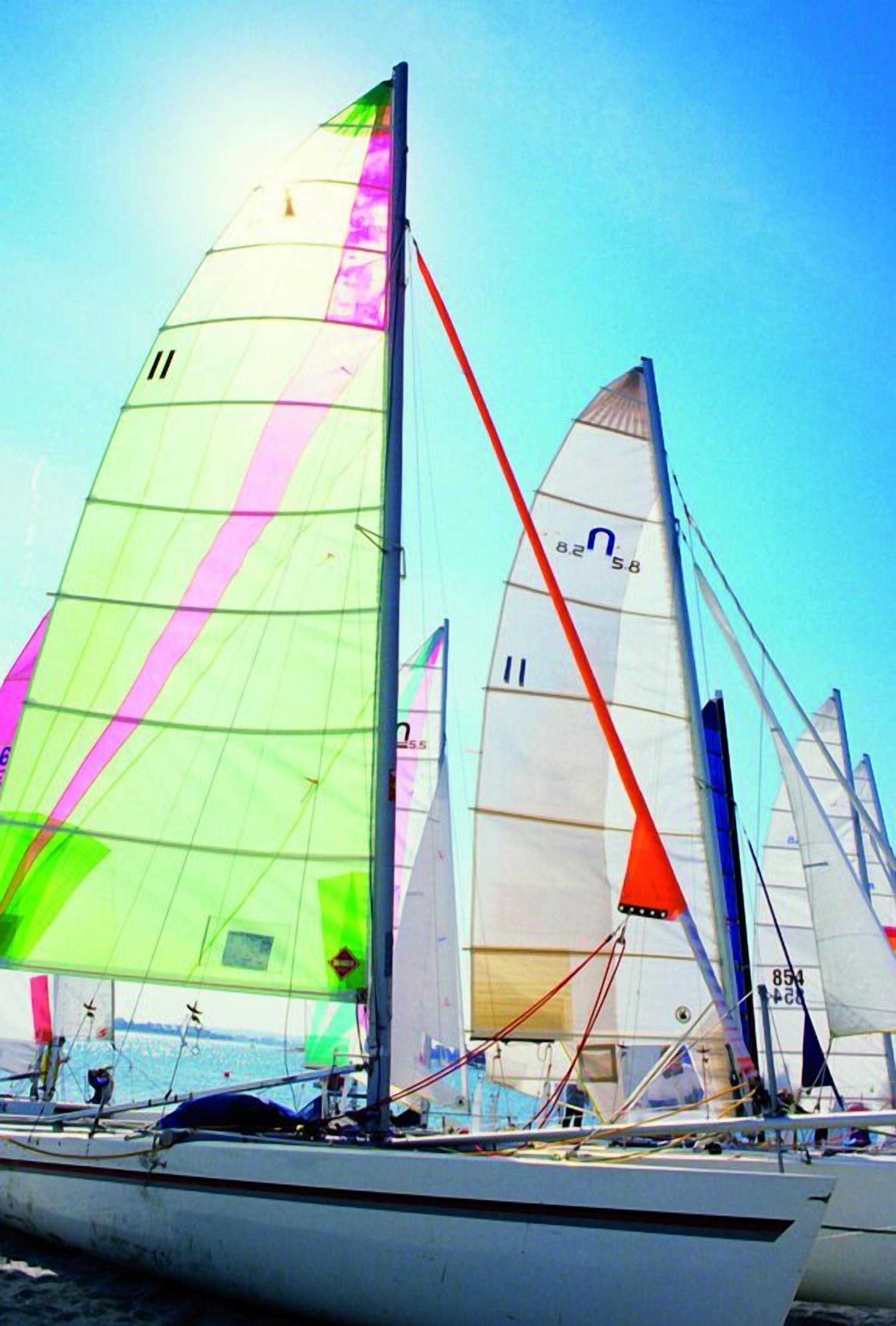 Un velero con varias velas, incluyendo una vela roja destacada y una vela verde con franjas rosadas.