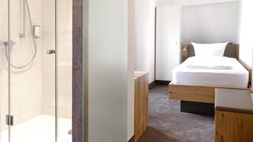 Ein Hotelzimmer mit Dusche, einem Bett, einem Nachttisch und einer Holzbank.