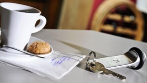 A white mug, a cookie, a key, and a piece of paper with a stamp on a table. - Hotel Gasthof Zur Linde (Hessdorf)