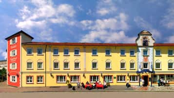 A hotel with a red and yellow facade, multiple windows, and a central entrance with a decorative arch.