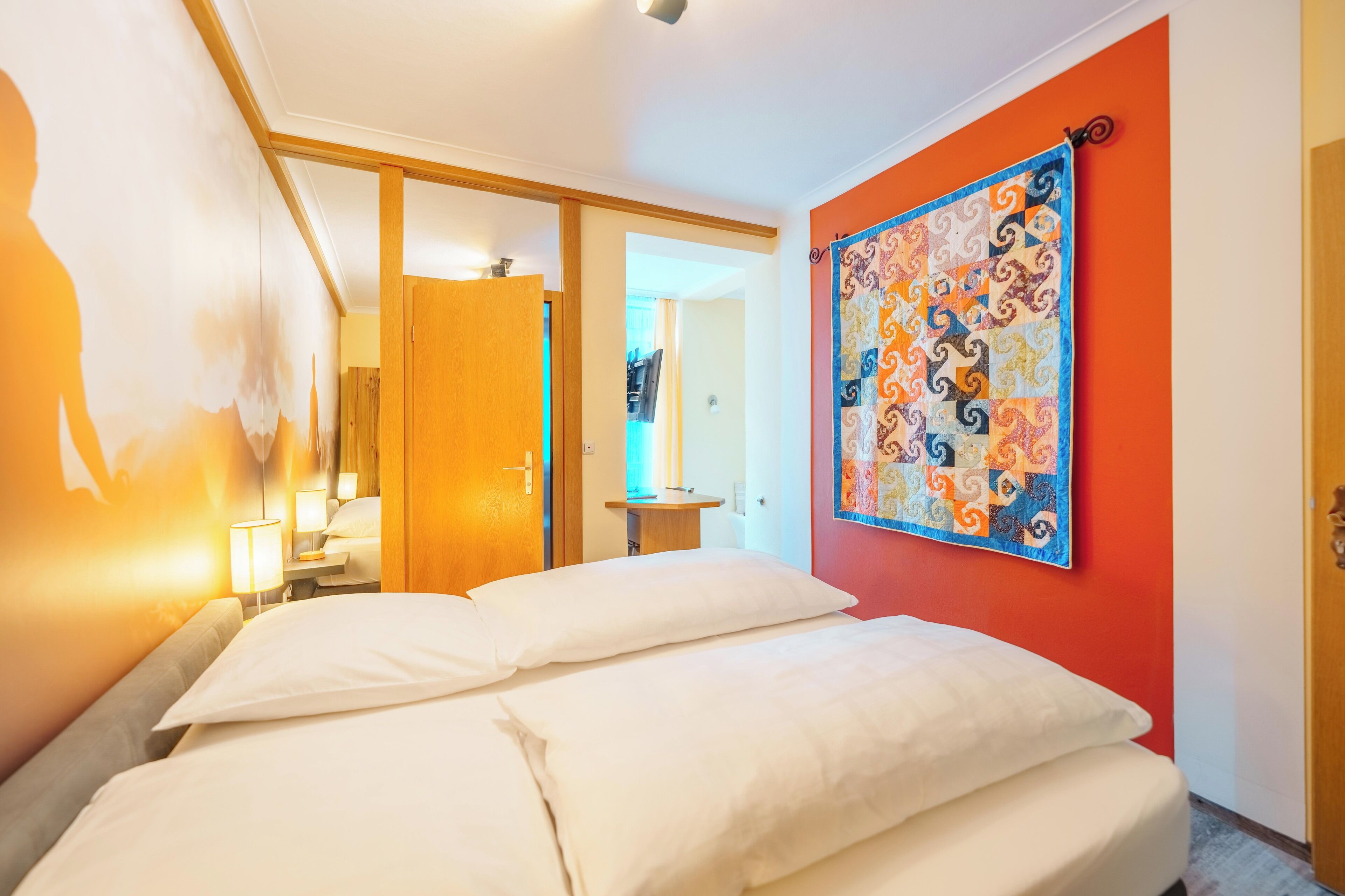 Una habitación de hotel con una cama, un cuadro en la pared y una puerta que da a otra estancia.