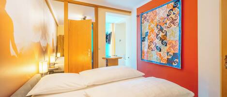 Una habitación de hotel con una cama, un cuadro en la pared y una puerta que da a otra estancia.