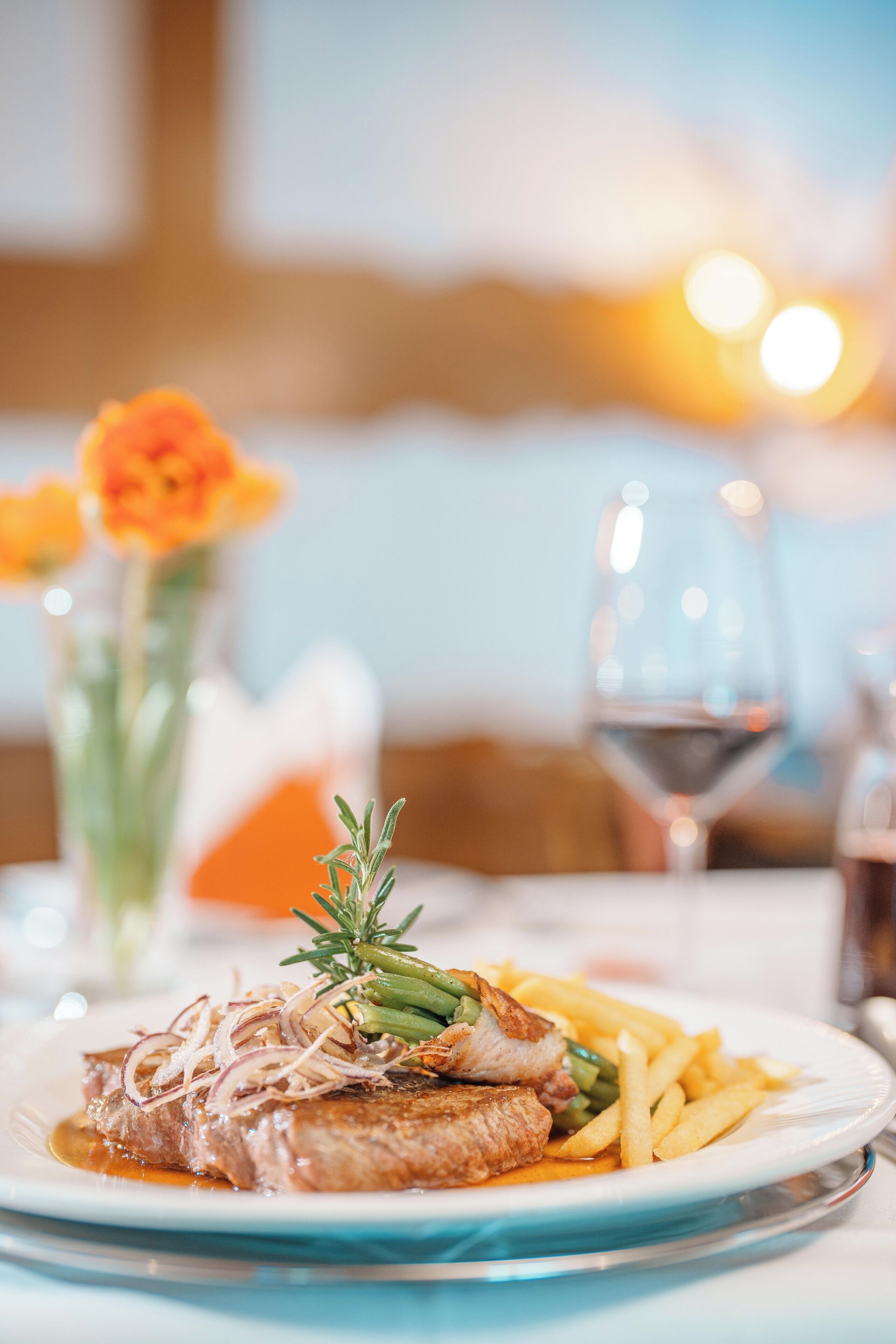 Un plato de comida con bistec, papas fritas y verduras, acompañado de una copa de vino.