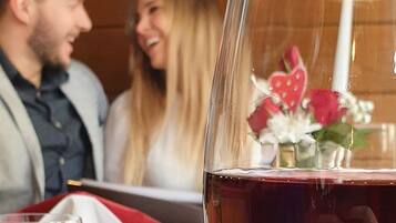 Primer plano de una copa de vino, una vela, un paño rojo y un jarrón pequeño con flores sobre una mesa.