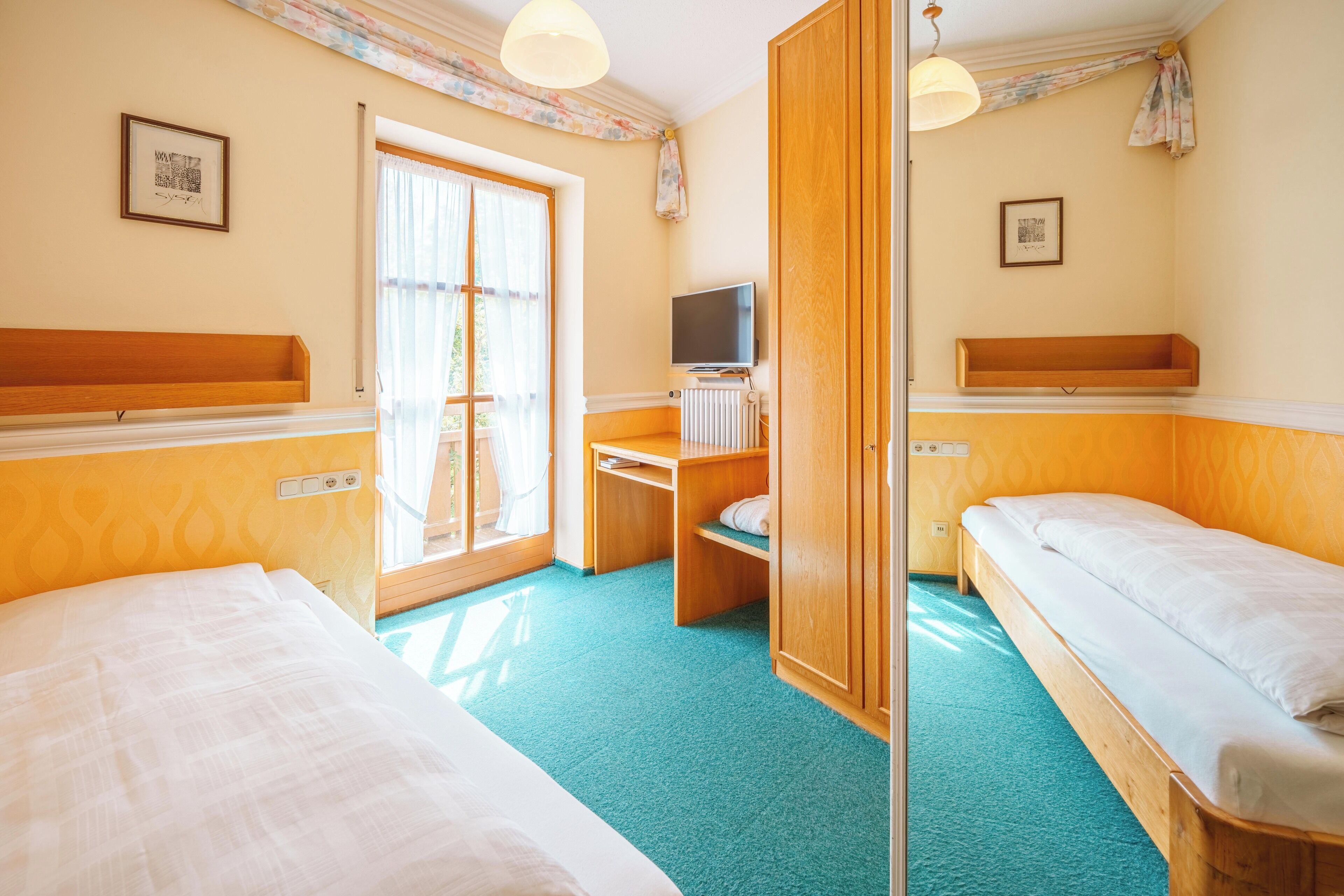 Une chambre d’hôtel avec deux lits, un bureau avec une télévision, une armoire en bois et une fenêtre avec des rideaux.