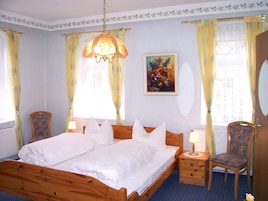 Quarto com uma cama de madeira, duas mesas de cabeceira com abajures, uma cadeira e um quadro na parede.
