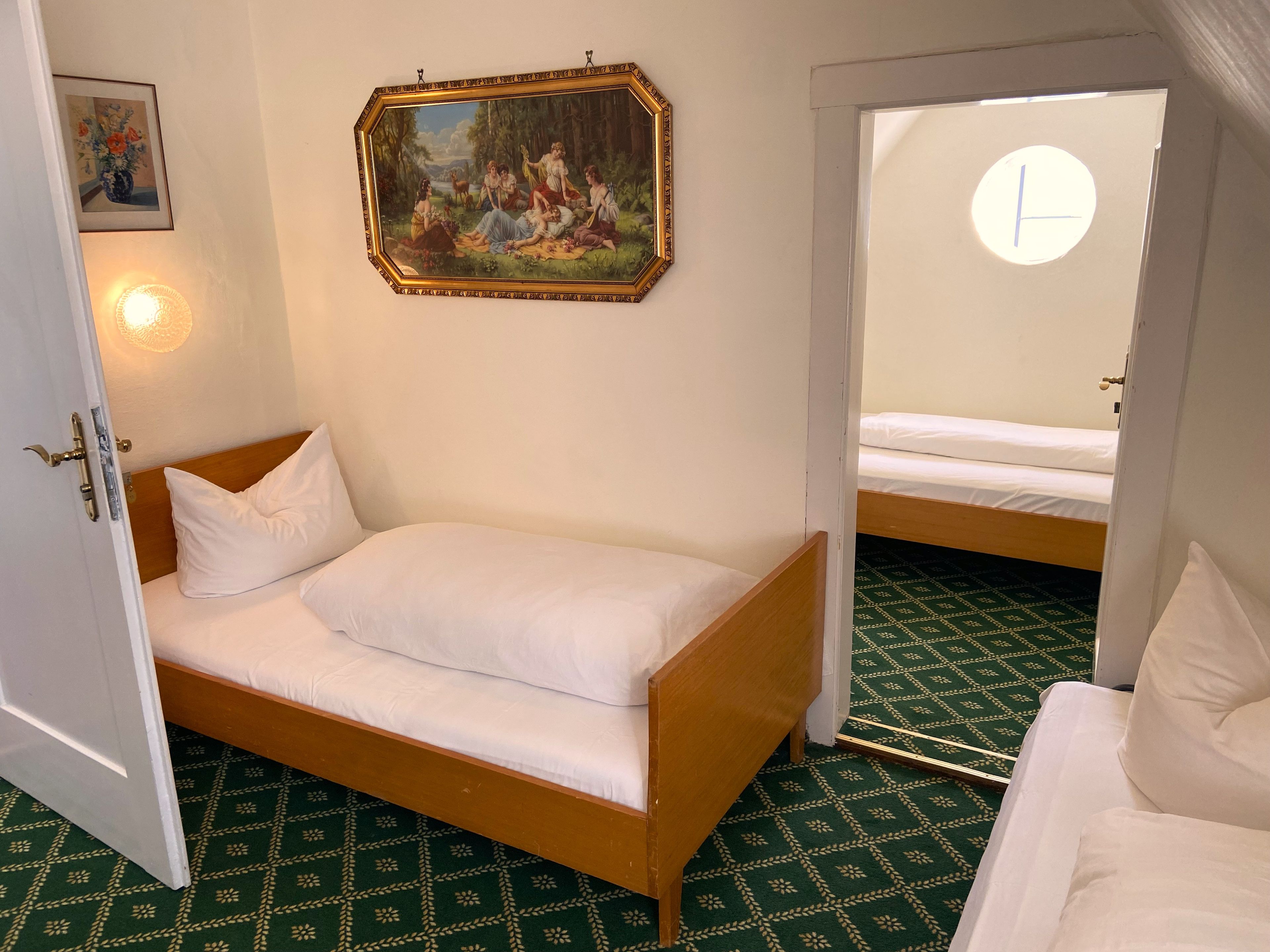 A room with a single bed, a painting on the wall, and a door leading to another room.