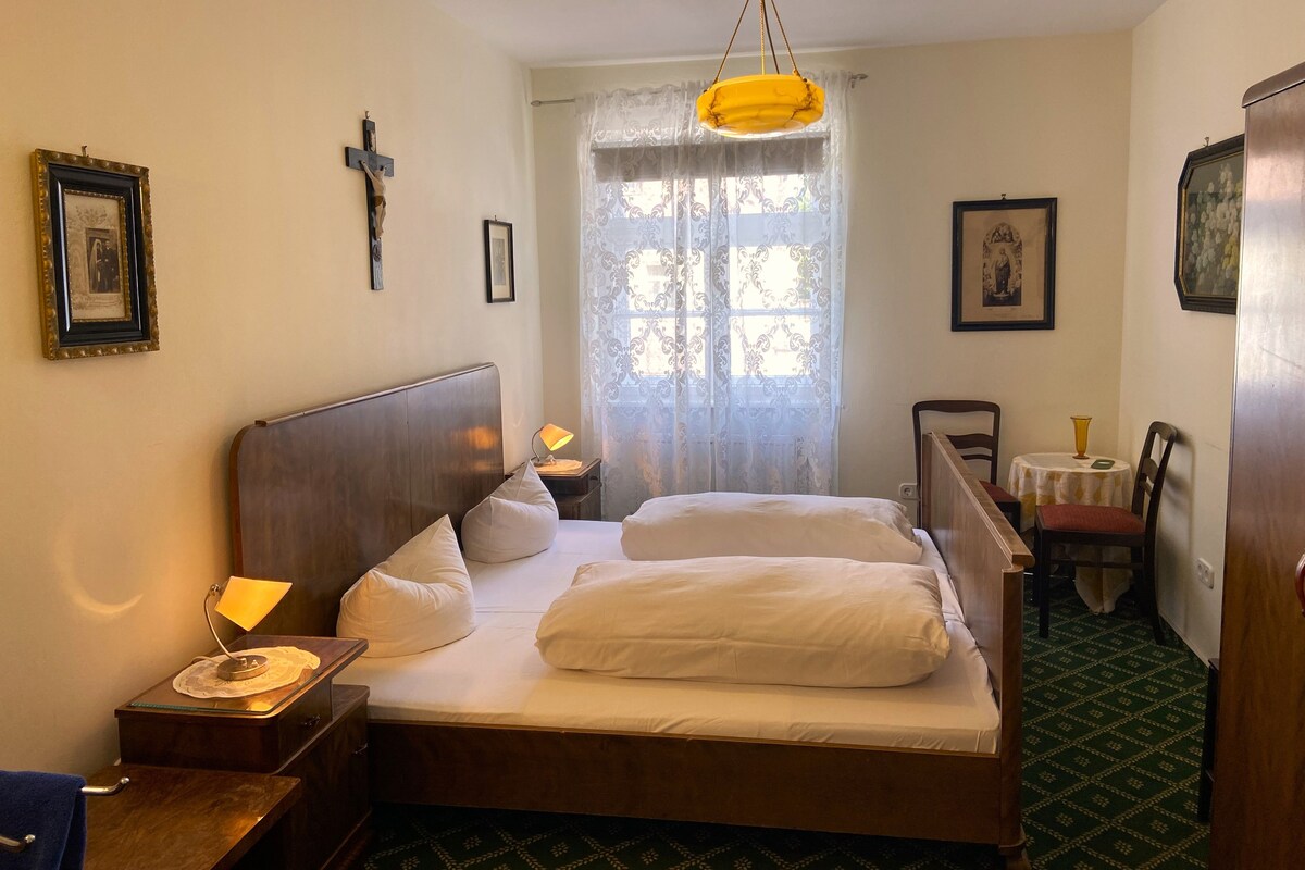 Una habitación de hotel con cama, mesitas de noche, escritorio, silla y ventana con cortinas.