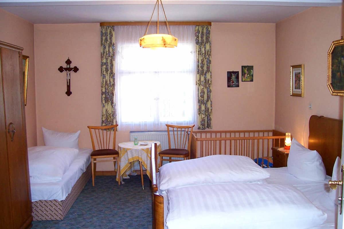 Habitación de hotel con dos camas individuales, una mesita con sillas, un radiador y una ventana con cortinas.