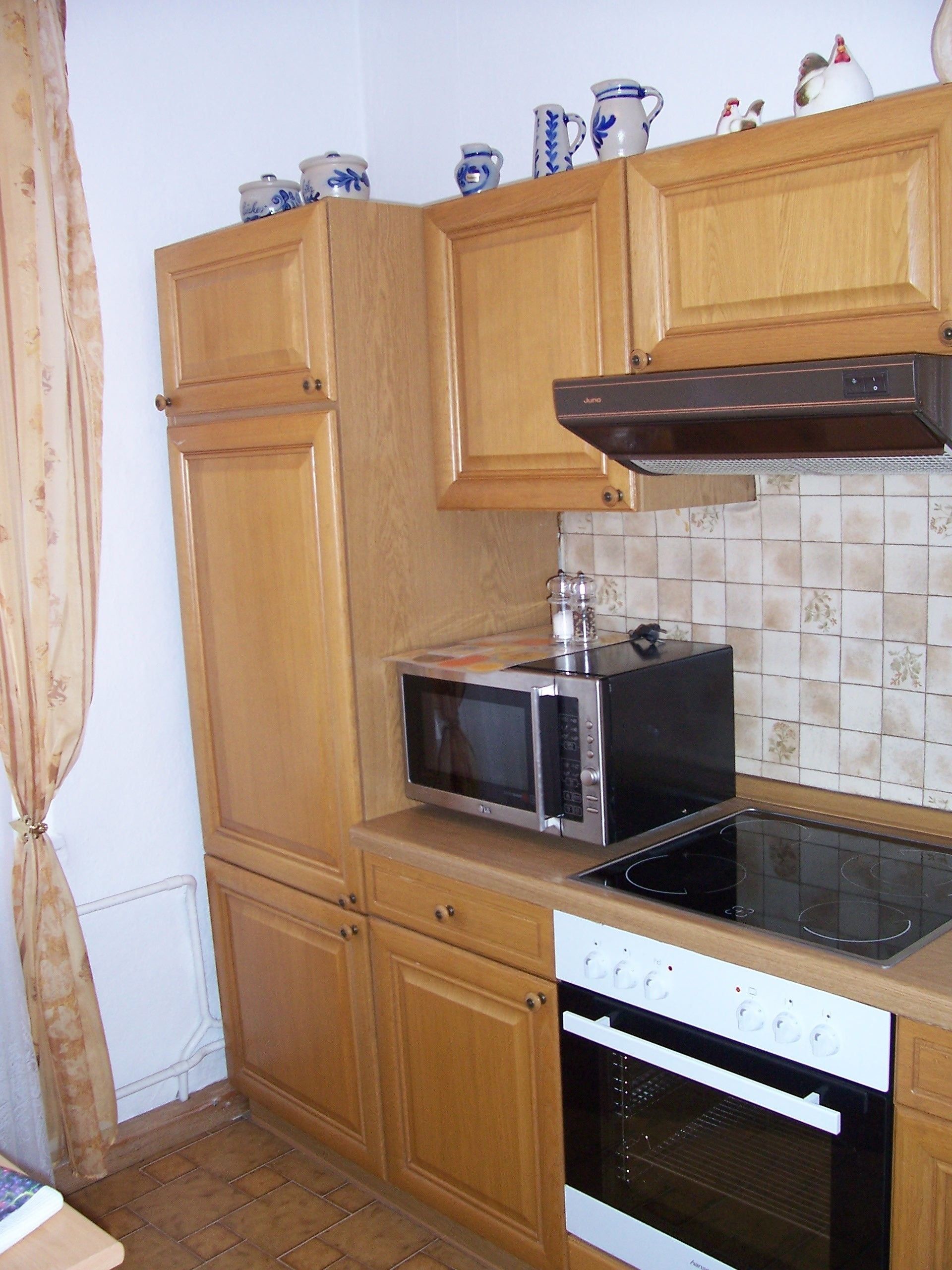 Een keuken met houten kastjes, een magnetron, een oven en een betegelde achterwand.
