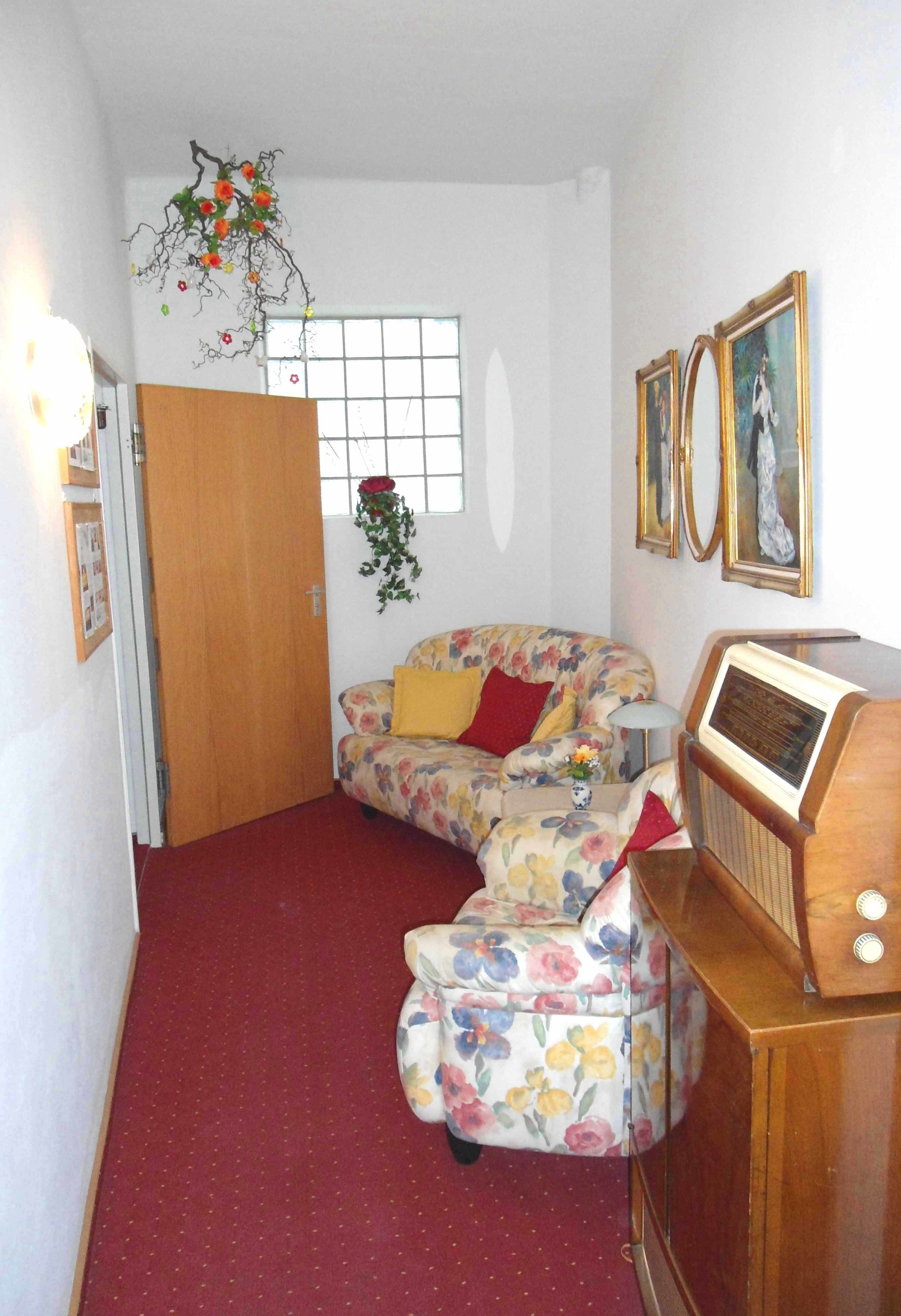 Ein kleiner, gemütlicher Raum mit einem blumigen Sofa, einem Holzschrank mit einem Radio und einem Fenster mit Blick.