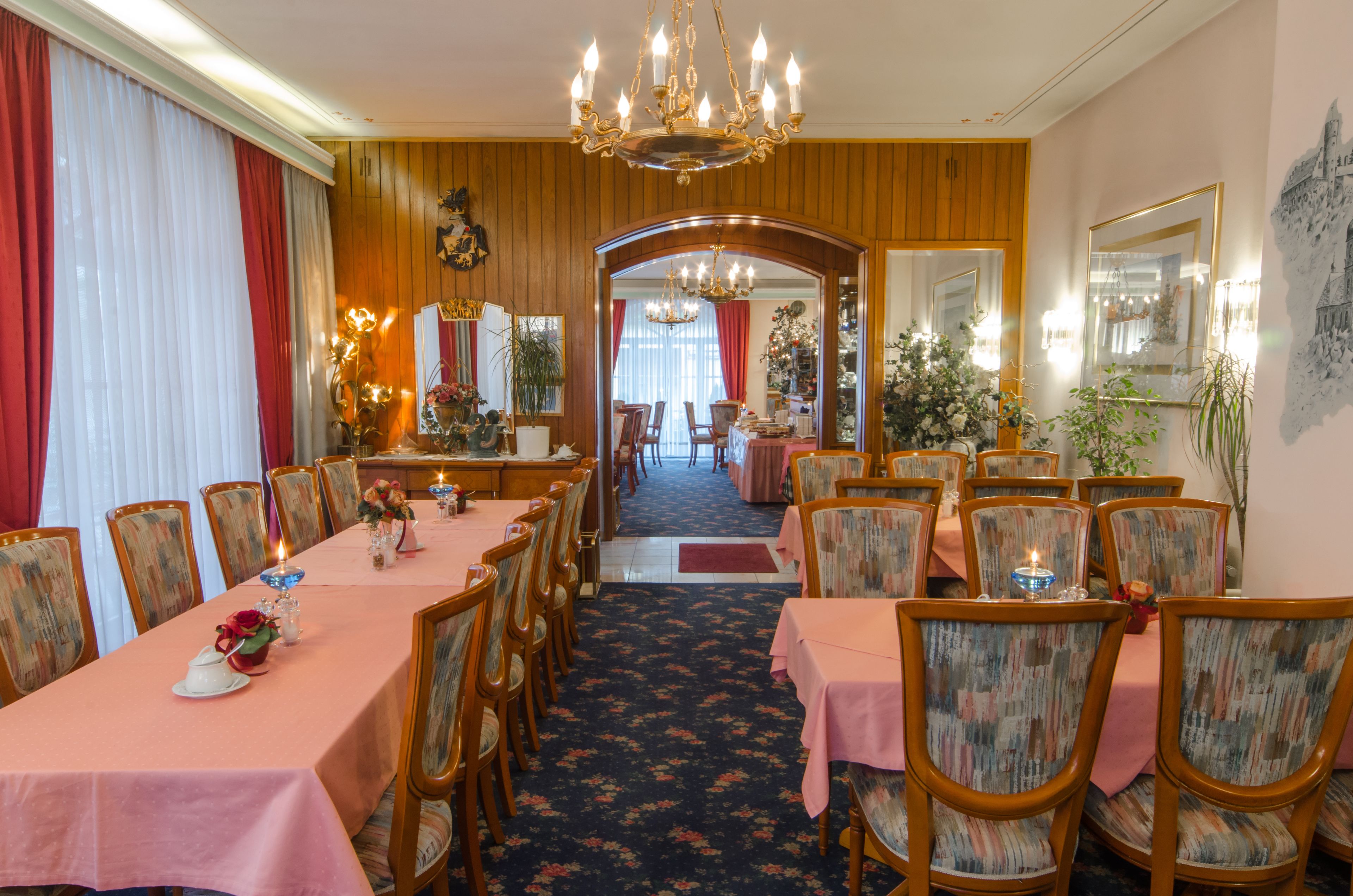 Uma sala de jantar formal com painéis de madeira, um lustre e mesas postas para refeição.
