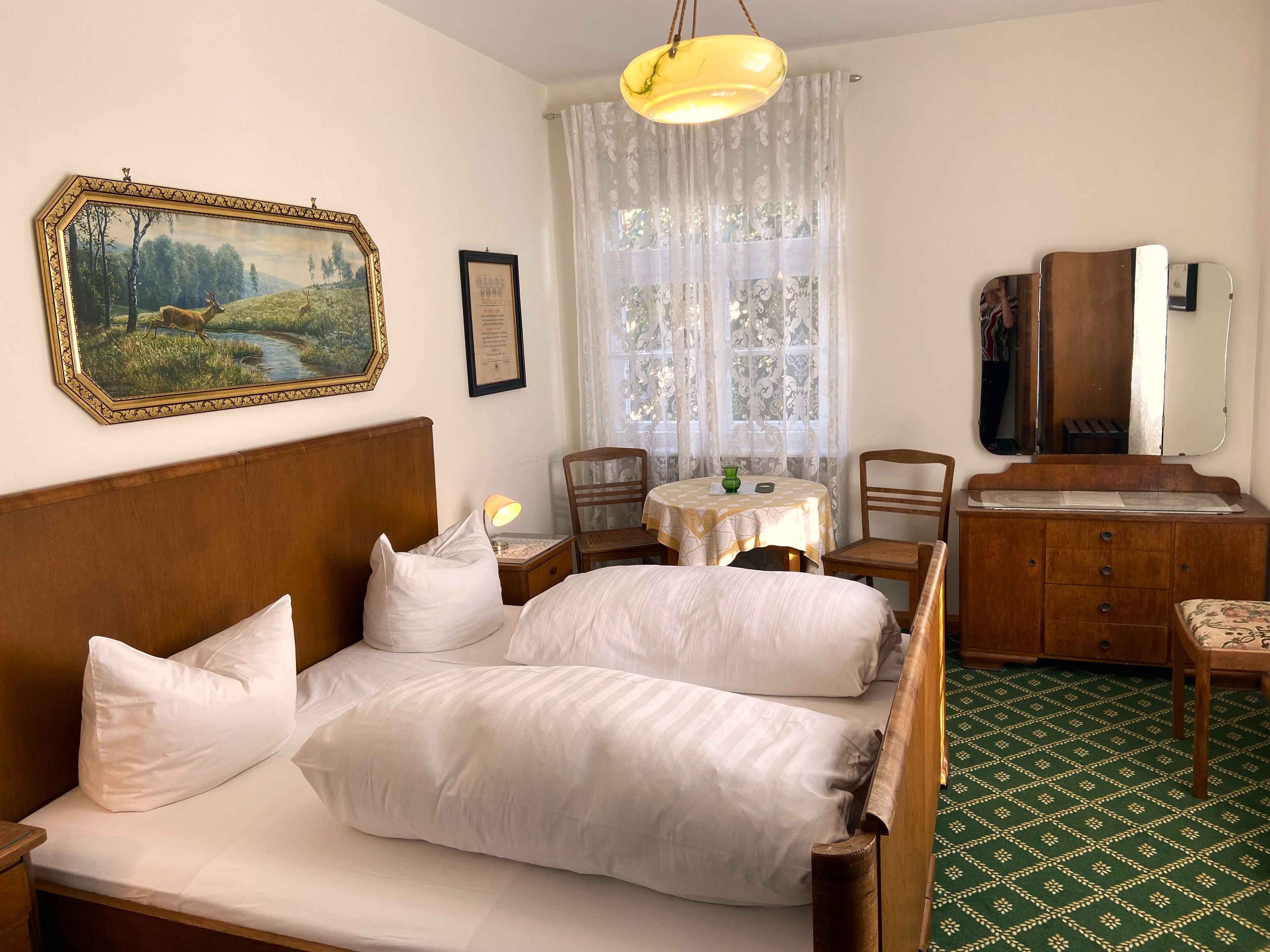 Habitación de hotel con cama doble, escritorio con silla, una mesita, un espejo y un cuadro en la pared.