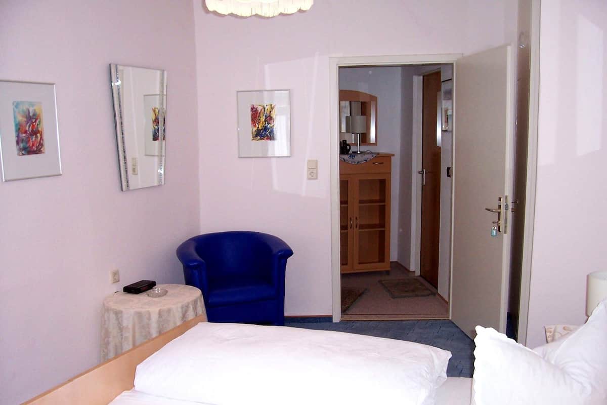 Una habitación de hotel con una cama, un sillón azul, una mesita pequeña y un armario.