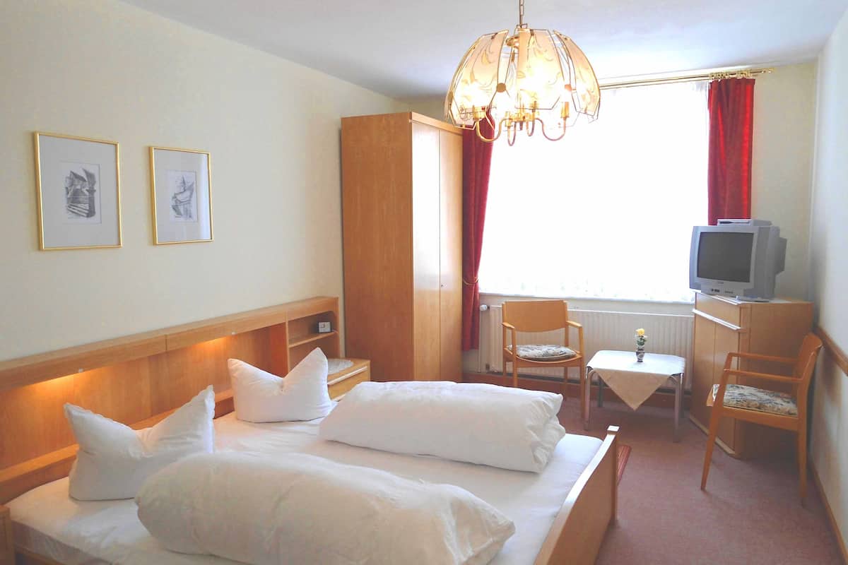 Habitación de hotel con cama doble, un escritorio con silla, un televisor y dos cuadros en la pared.