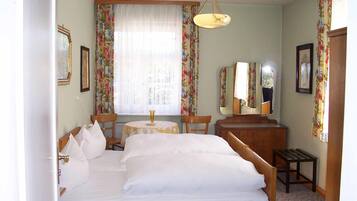 Une chambre d’hôtel avec un grand lit, une petite table, une chaise, un bureau, un miroir et des rideaux à motifs floraux.