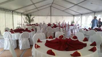 Un espacio para eventos con carpas, mesas redondas cubiertas con manteles blancos y servilletas rojas, sillas blancas y candelabros.