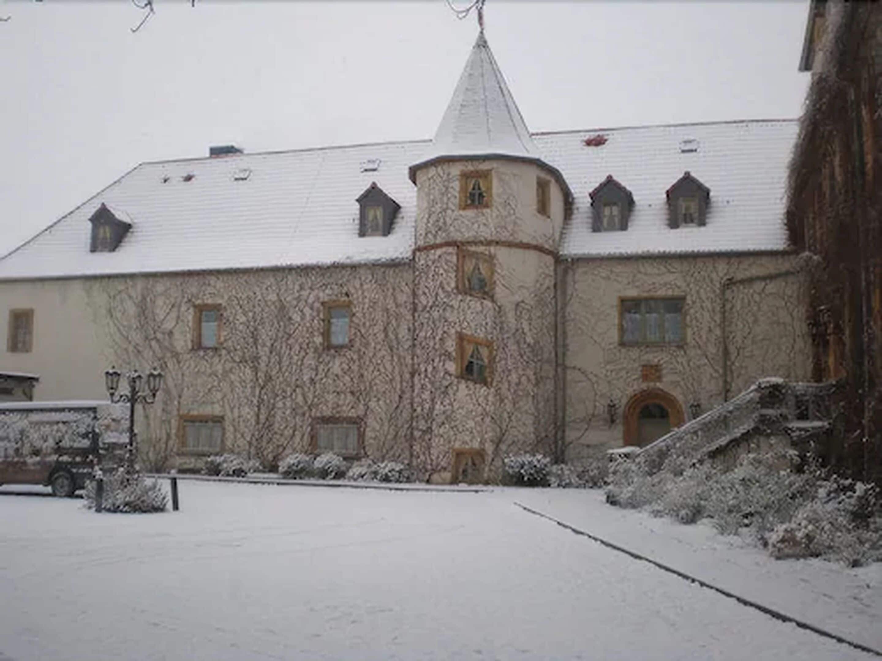 Um edifício coberto de neve com uma torre central, várias janelas e uma área pavimentada em frente.