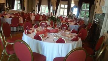 Un salón de banquetes con mesas redondas, sillas rojas y manteles blancos.