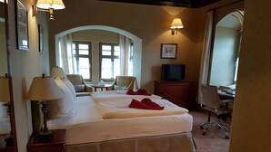 Una habitación de hotel con una cama grande, dos sillas, un escritorio, un televisor y un espejo.