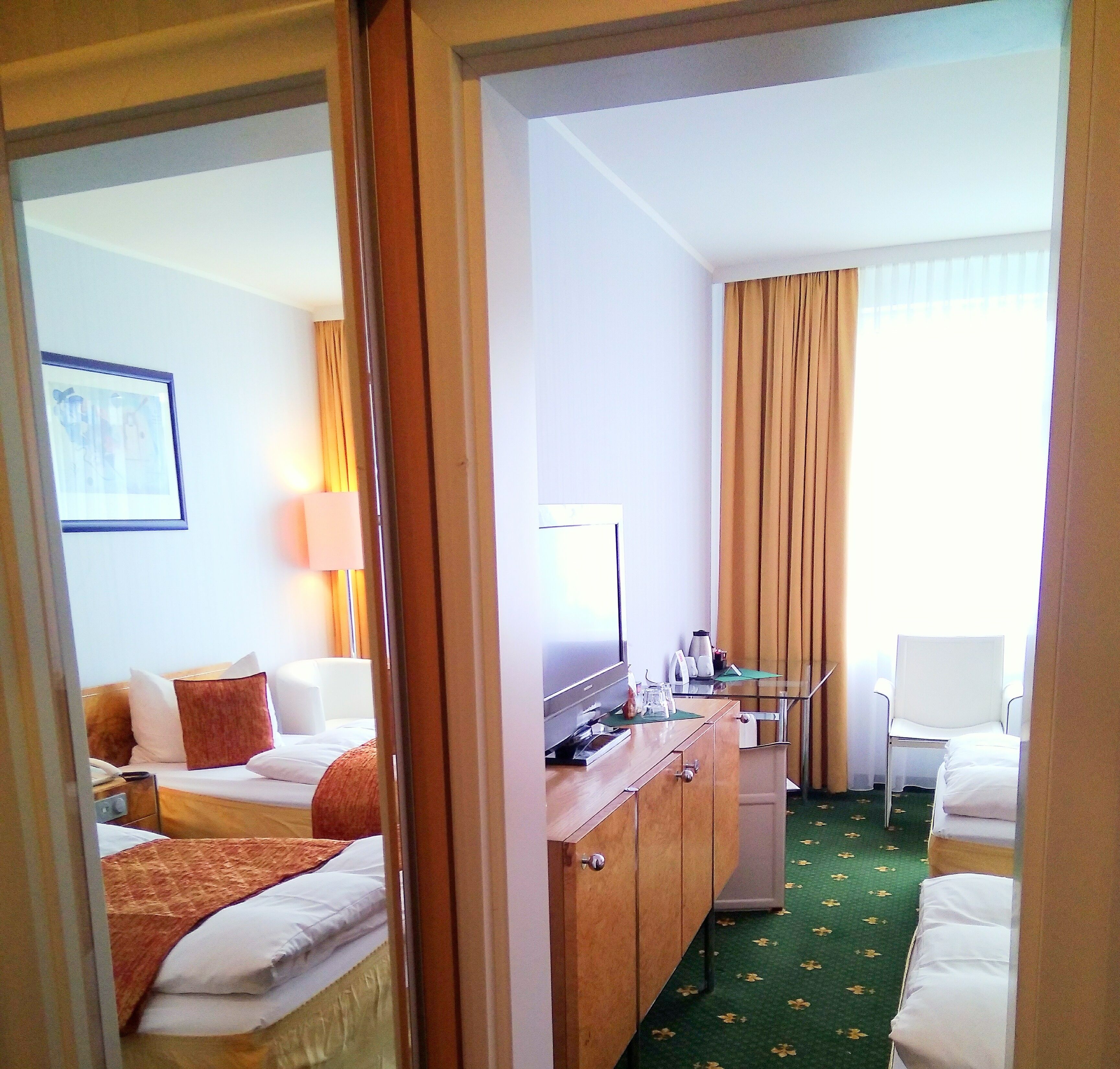 Habitación de hotel con cama, escritorio, silla, espejo y ventana con cortinas.