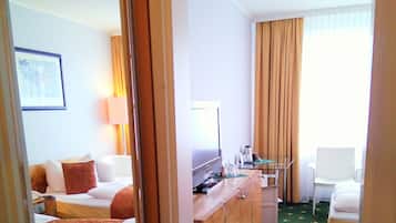 Habitación de hotel con cama, escritorio, silla, espejo y ventana con cortinas.