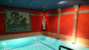 A swimming pool with clear blue water, surrounded by red walls and a mosaic. - Alexa Hotel (Göhren)
