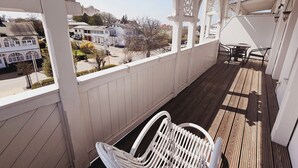 A covered porch with a white chair, wooden flooring, and a view of residential buildings. - Alexa Hotel (Göhren)