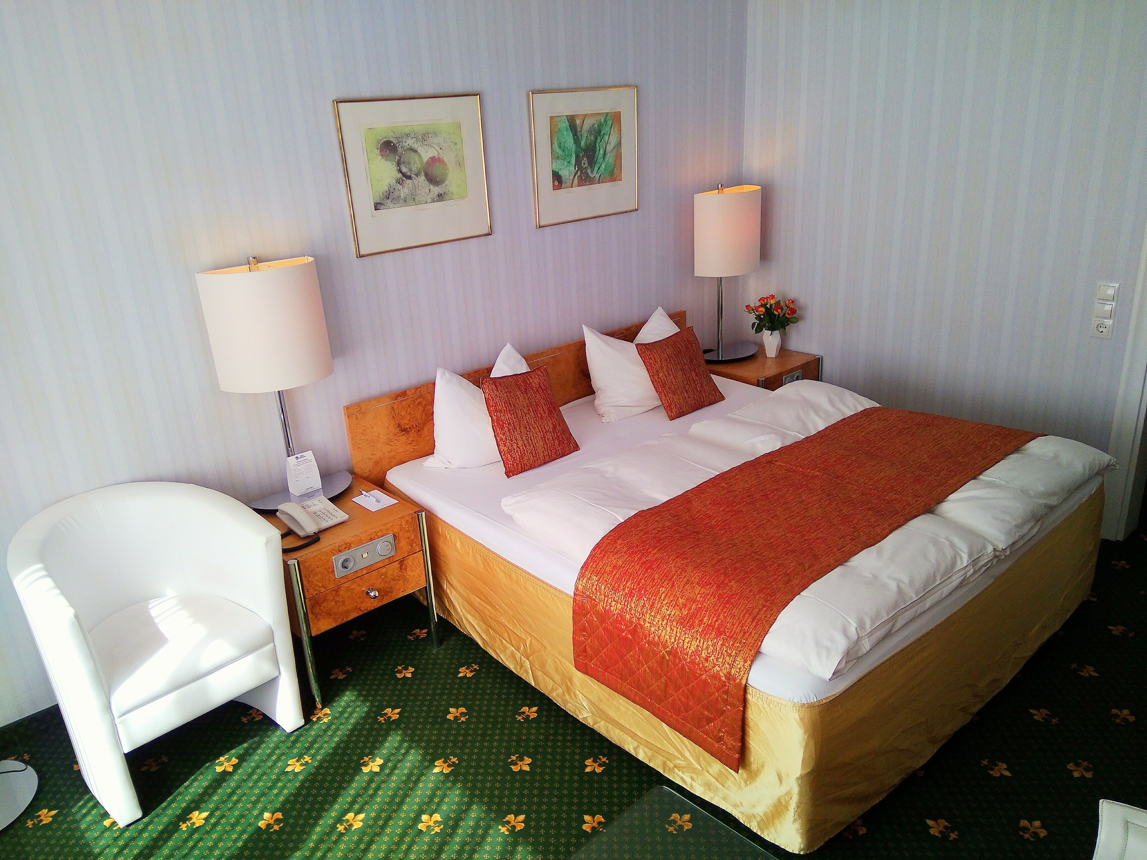 Una habitación de hotel con una cama, una silla, dos mesitas de noche y dos lámparas de pared.