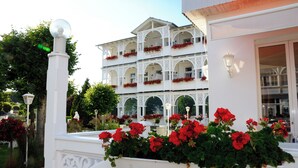 A hotel with a white exterior, multiple balconies with red flowers, and a white railing. - Alexa Hotel (Göhren)