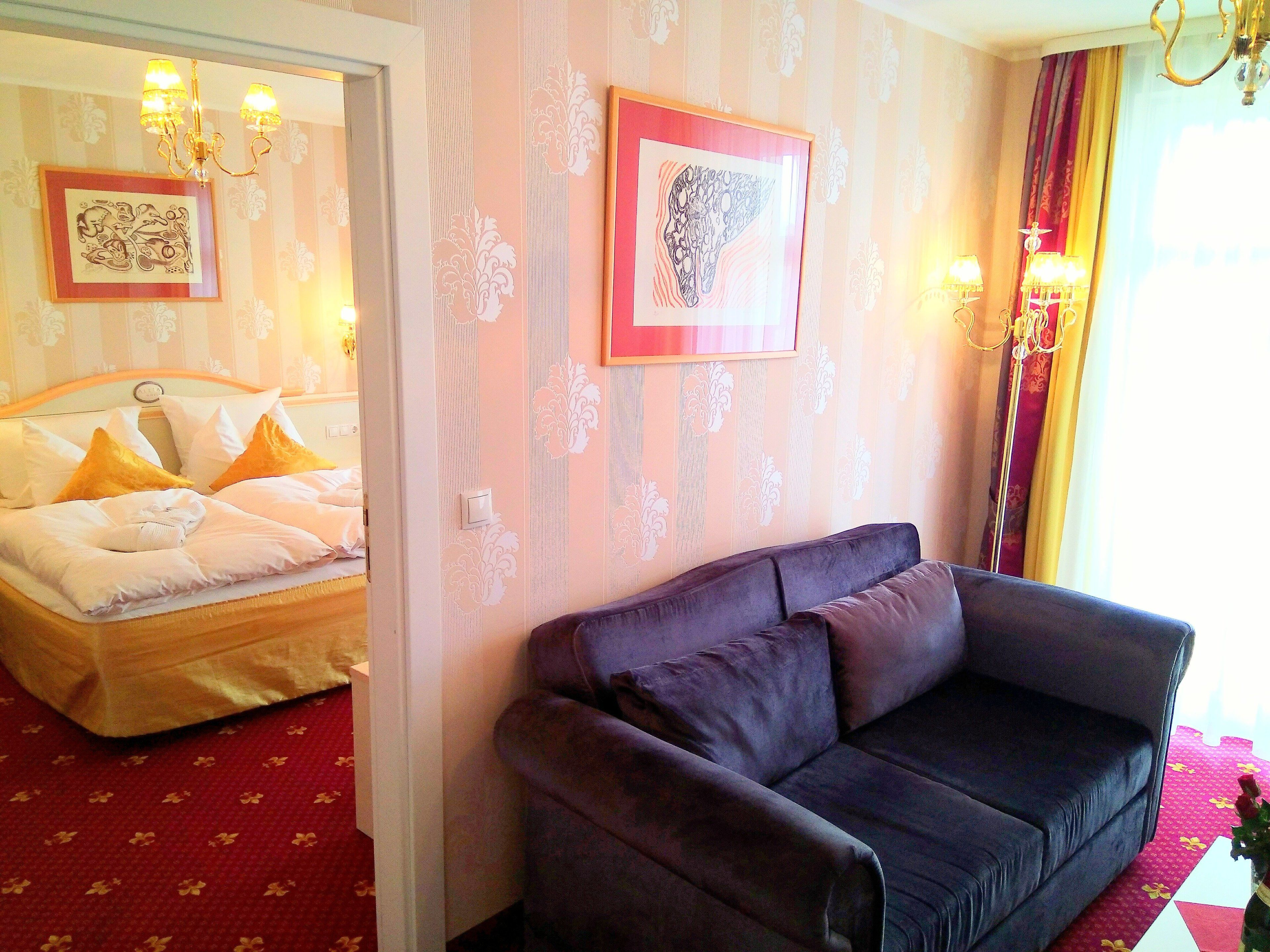 Ein Hotelzimmer mit einem Bett, einem violetten Sofa und zwei gerahmten Kunstwerken an der Wand.