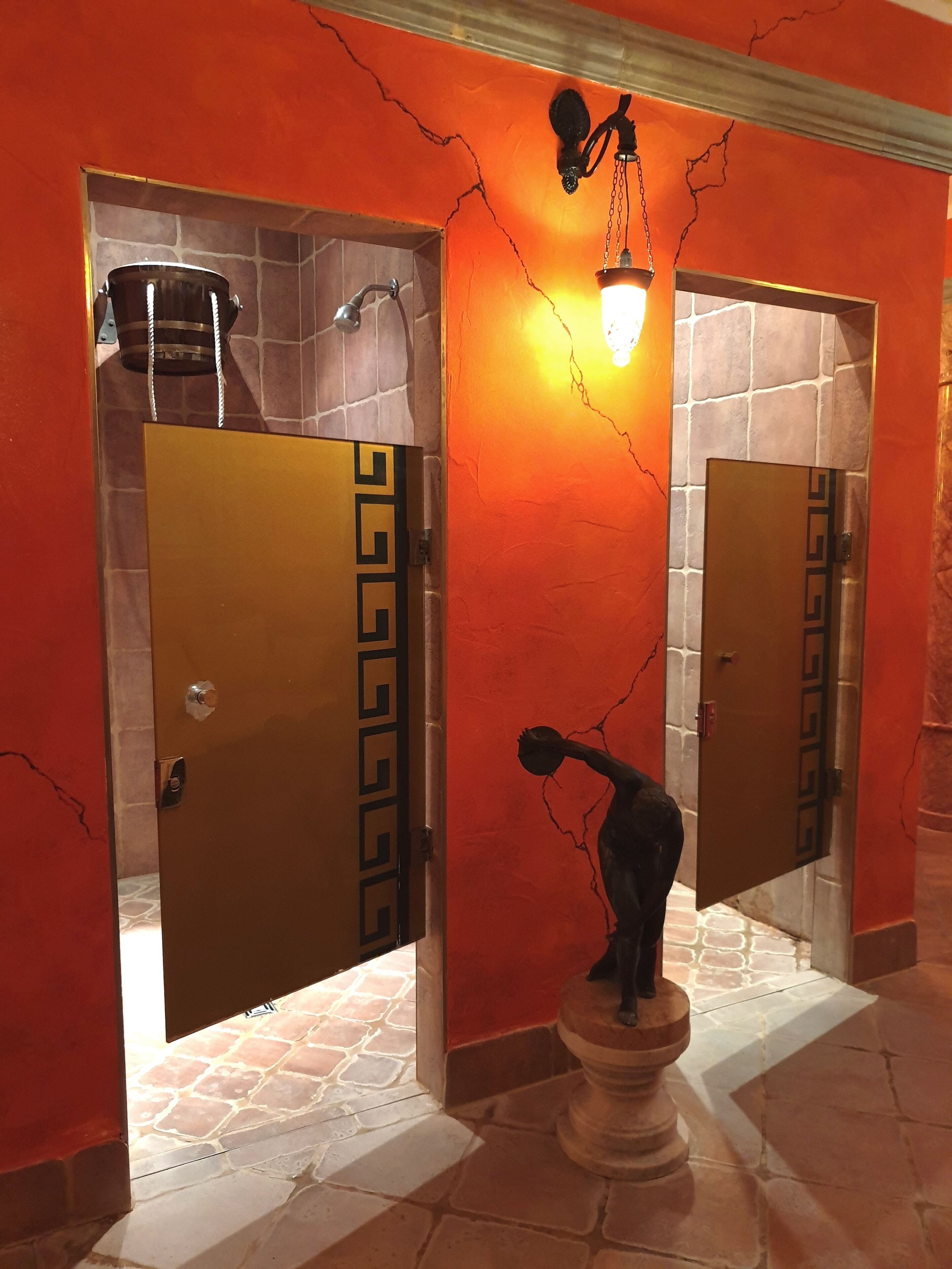 A bathroom with two doors featuring a geometric pattern, a statue on a pedestal, and a crack running along the wall.