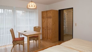 A bedroom with a bed, a wooden wardrobe, a dining table with chairs, and a shower area. - Hotel Mönter-Meyer (Bad Laer)