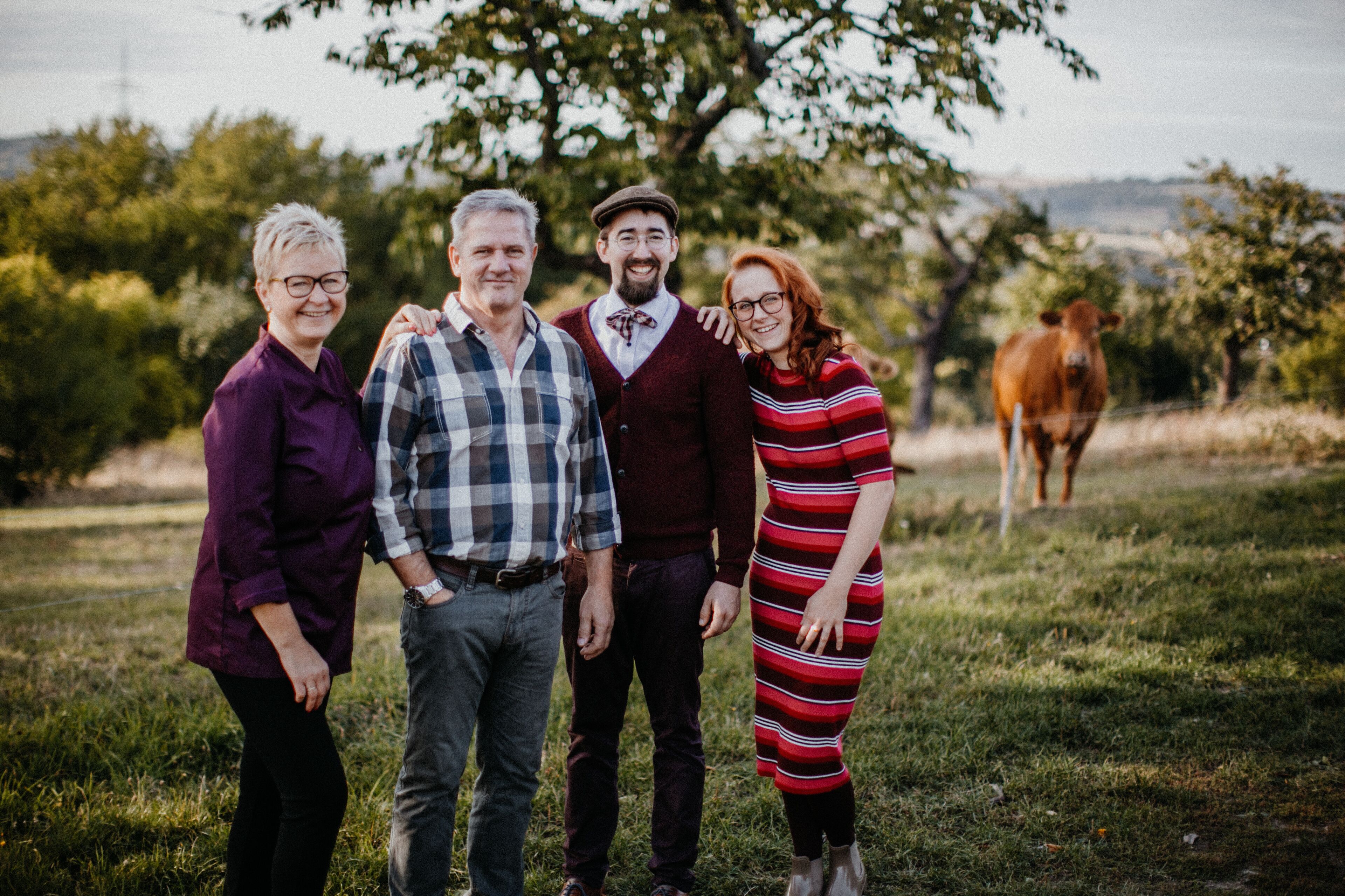 Un groupe de personnes se tient dans un champ herbeux, avec des arbres et une vache en arrière-plan.