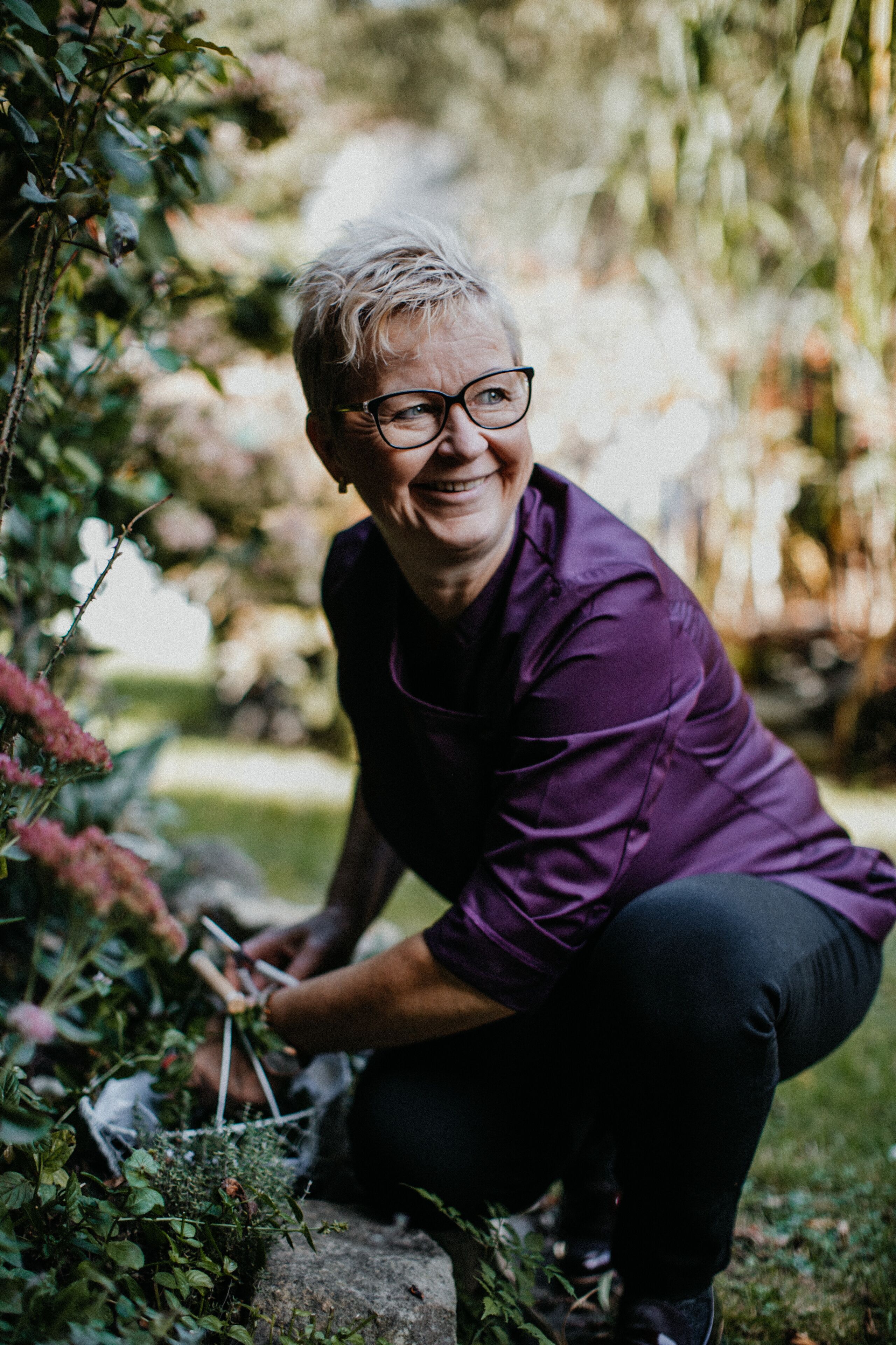 A person crouching in a garden, surrounded by greenery and plants.